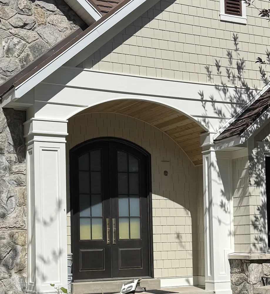 Arched dark iron double entry doors with glass panels under a white portico